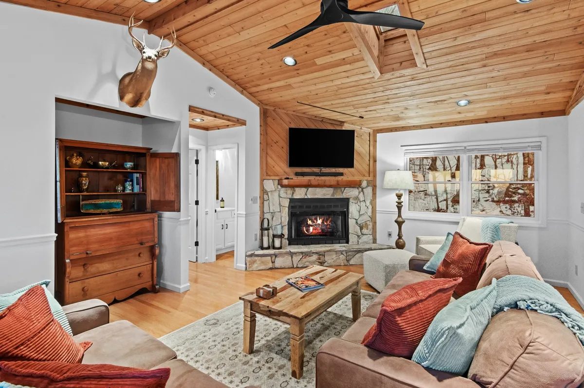 A cozy living area with a stone fireplace as the focal point, surrounded by plush sofa seating and a wooden coffee table. Decorative wall art and expansive windows frame the mountain vistas outside, creating a warm and inviting atmosphere.