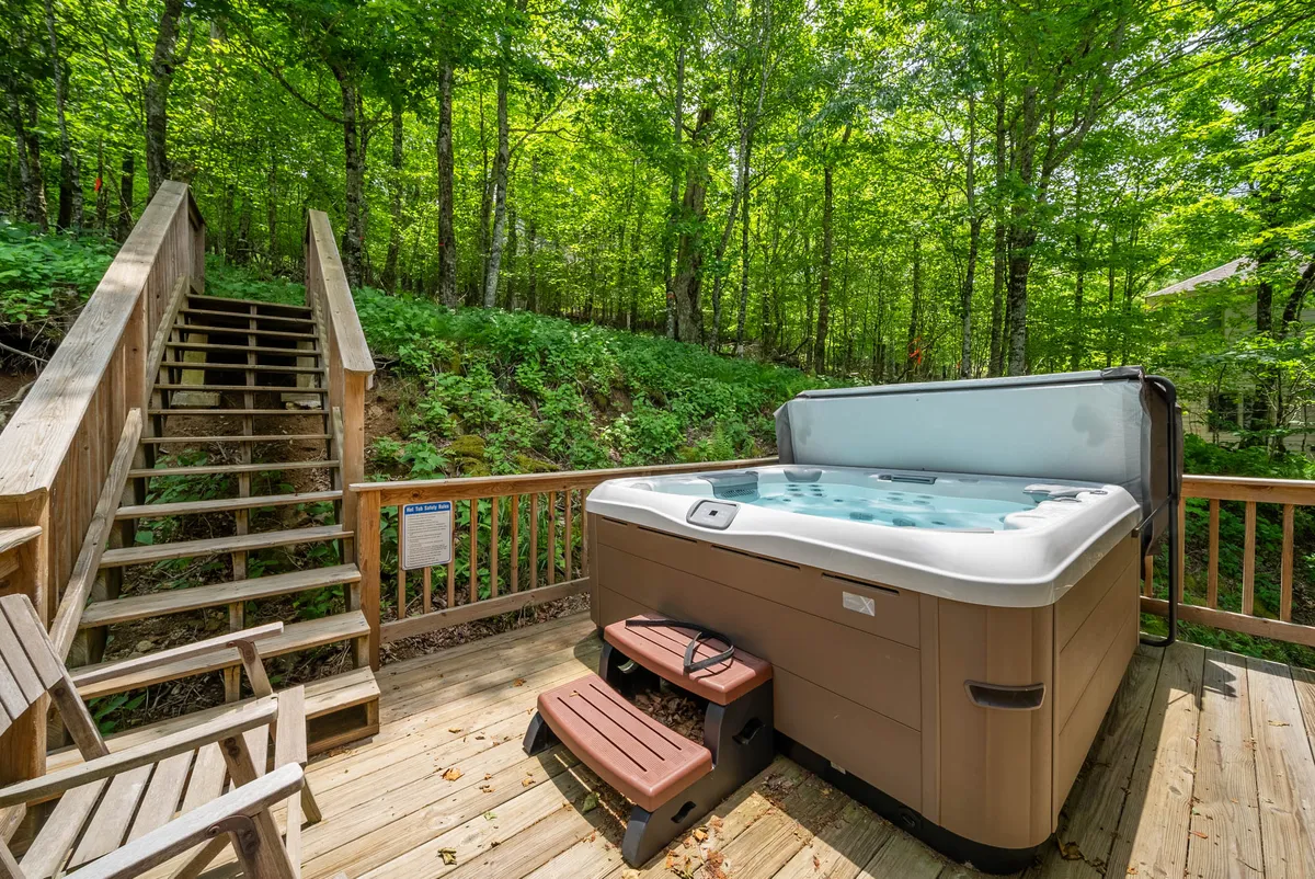 A serene exterior setting with a private hot tub on a wooden deck surrounded by trees. The inviting hot tub and peaceful natural backdrop evoke relaxation after a day of outdoor activities like skiing, hiking, or biking.