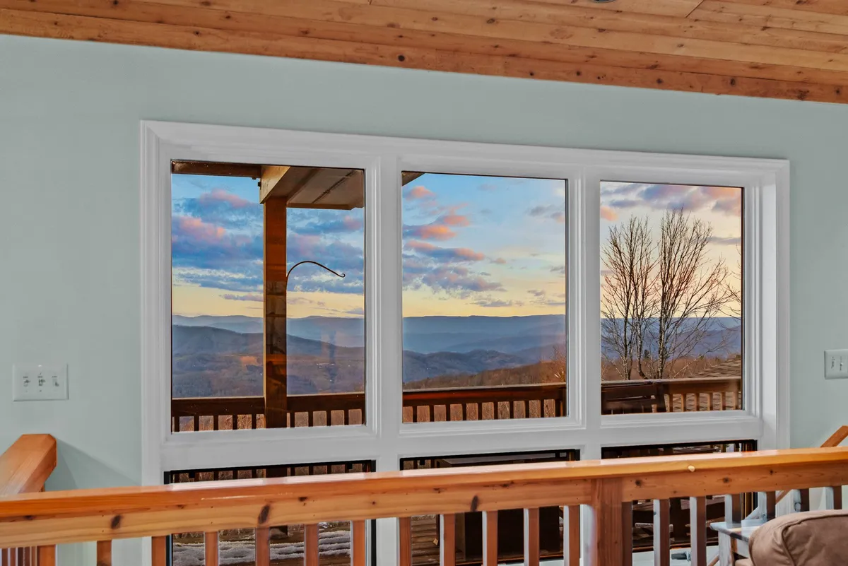 A stunning view from the property overlooks a vast mountain landscape at sunset, framed by a wooden railing. The tranquil setting invites contemplation and appreciation of the surrounding beauty.