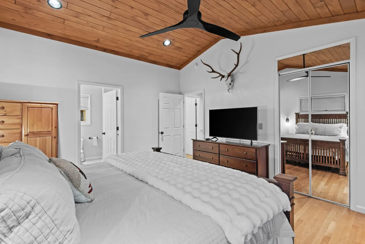 A cozy bedroom featuring a plush king-sized bed with inviting bedding, a wooden dresser, a large flat-screen TV, and decorative antlers on the wall. The atmosphere is serene and comfortable, ideal for relaxing and unwinding after a day in the mountains.