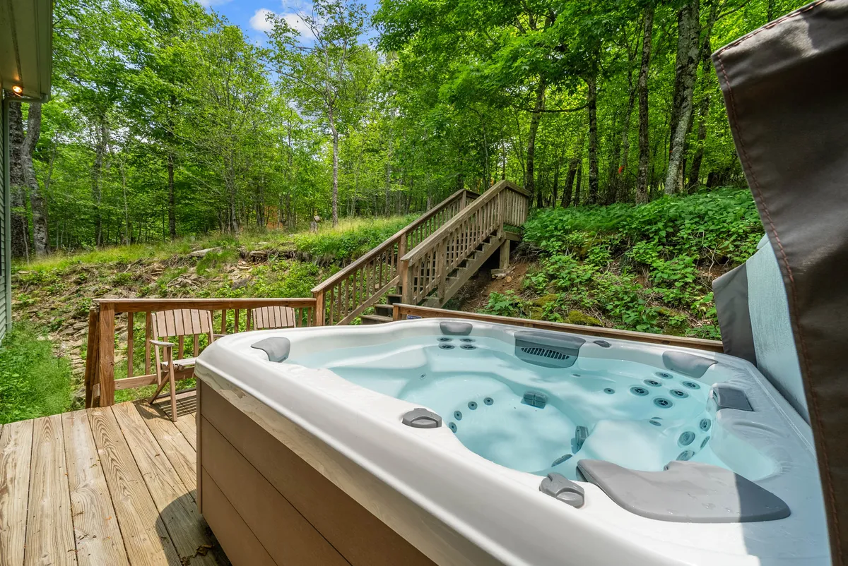 A tranquil scene showing a wooden deck with a private hot tub overlooking lush greenery. The setting is serene, inviting guests to relax in the hot tub while enjoying the surrounding nature. There's a strong sense of privacy and immersion in the outdoors, echoing the section's emphasis on relaxation under the stars.