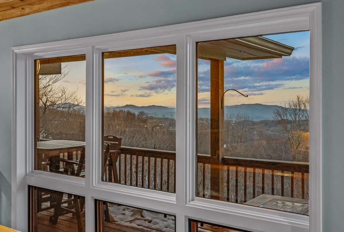 A tranquil interior space featuring expansive windows that frame a stunning sunset view, with comfortable outdoor furniture visible just beyond the glass. The scene exudes an atmosphere perfect for reflection, relaxation, or group gatherings, and hints at direct access to the outdoors.